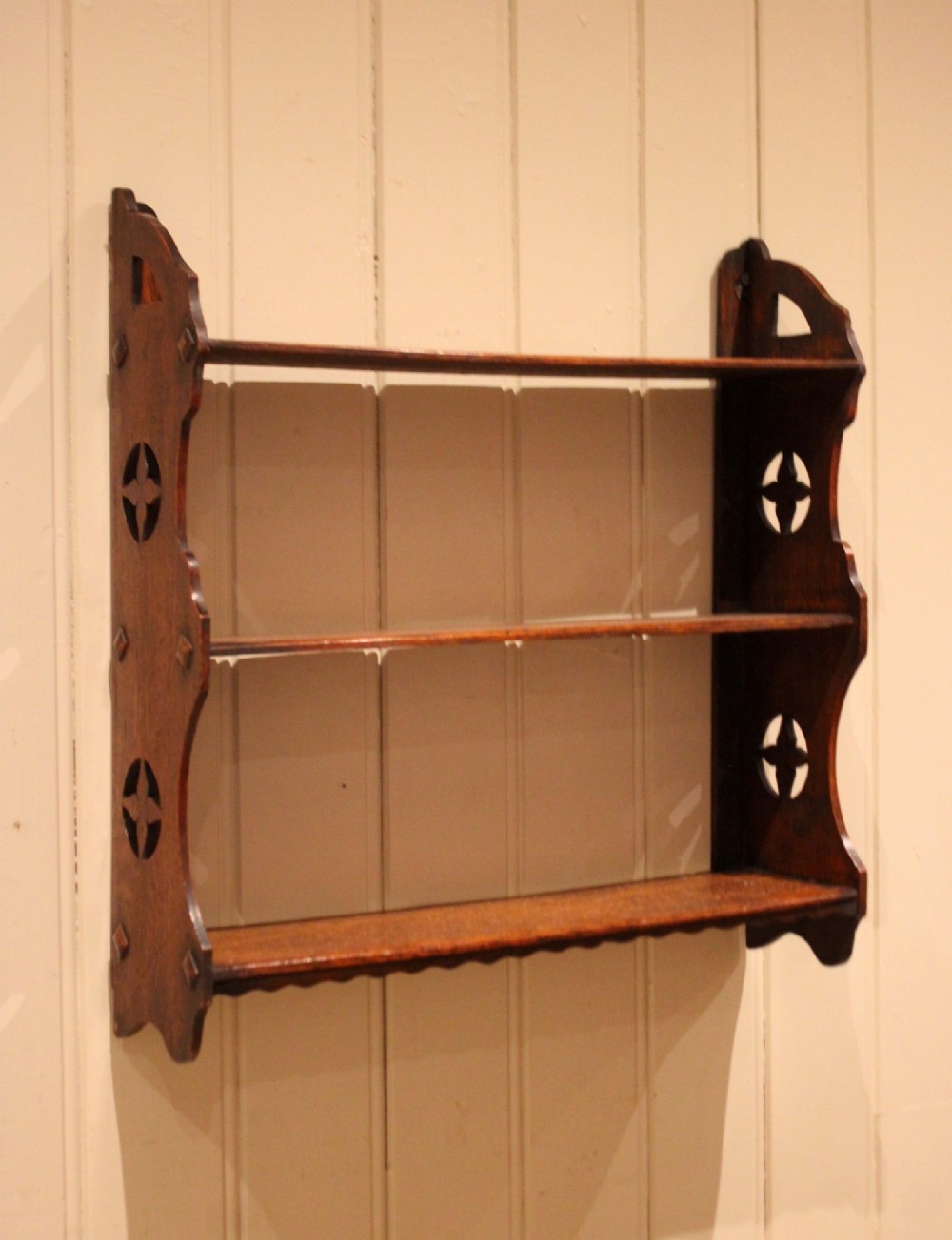 A late nineteenth-century dark oak wall-mounted shelf unit featuring three tiers and carved geometric cutouts along the side supports. View XI