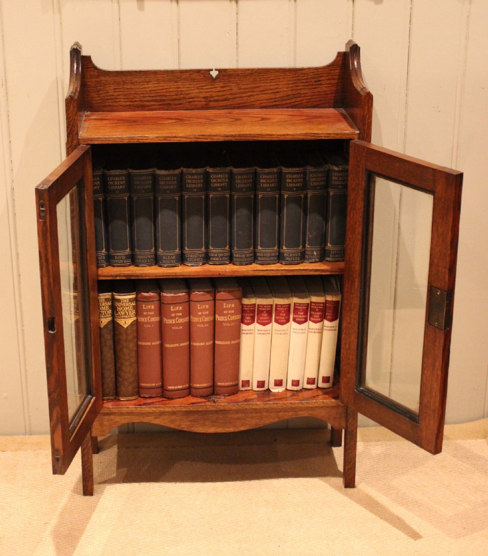 A small Arts and Crafts medium oak glazed bookcase featuring a gallery top with a pierced heart motif, two glazed doors, glazed side panels, and square legs. View XIII