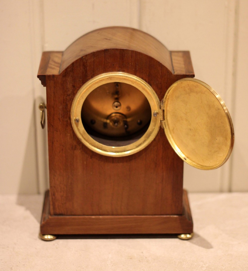 An Edwardian arched mahogany mantel clock featuring a shell motif inlay, a white dial with Roman numerals, brass side handles, and brass ball feet. View XII