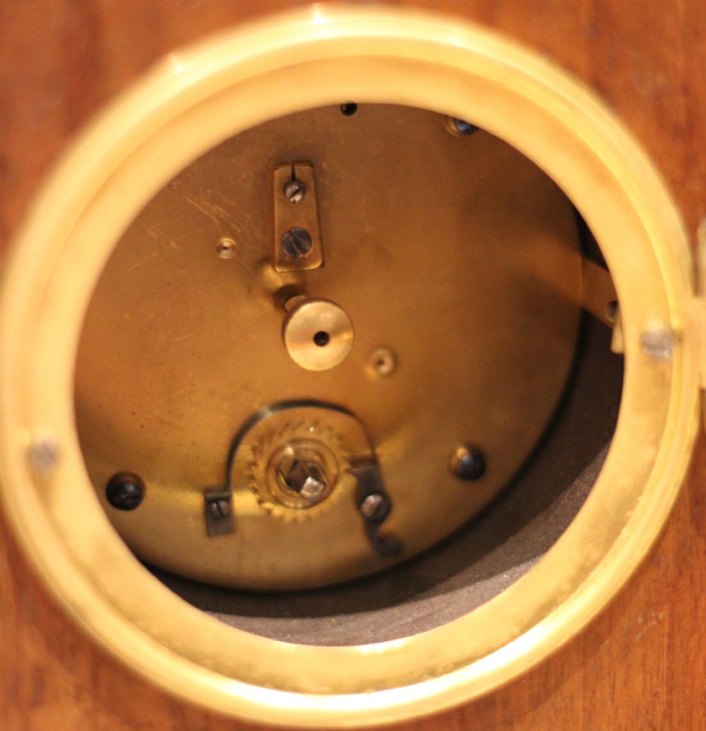 An Edwardian arched mahogany mantel clock featuring a shell motif inlay, a white dial with Roman numerals, brass side handles, and brass ball feet. View XIII