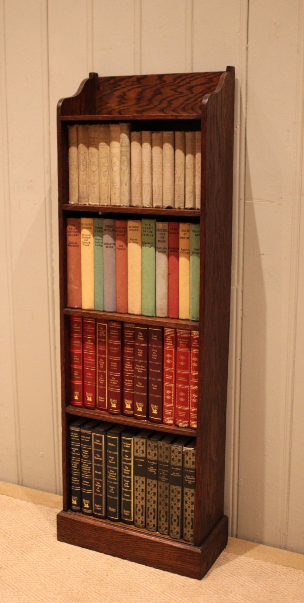 A tall, narrow dark oak open bookcase featuring multiple shelves, a shaped gallery top, and a solid plinth base. View V