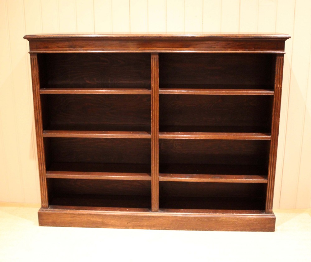 A double-bay open oak library bookcase featuring fluted pilasters, multiple horizontal shelves, a moulded top edge, and a solid plinth base. View II