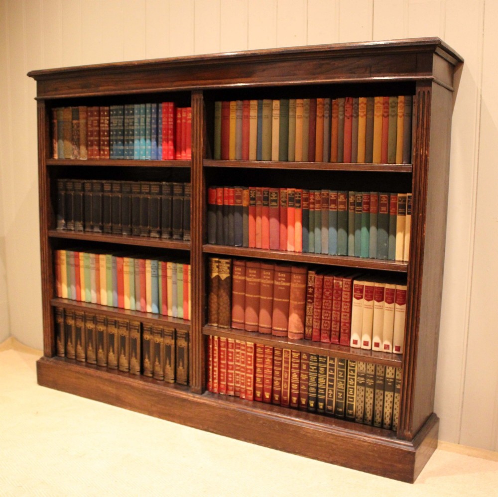 A double-bay open oak library bookcase featuring fluted pilasters, multiple horizontal shelves, a moulded top edge, and a solid plinth base. View V