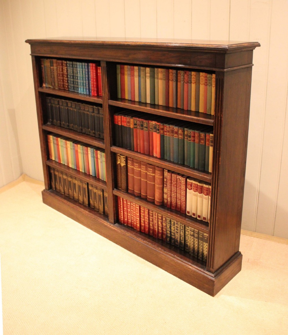 A double-bay open oak library bookcase featuring fluted pilasters, multiple horizontal shelves, a moulded top edge, and a solid plinth base. View VII