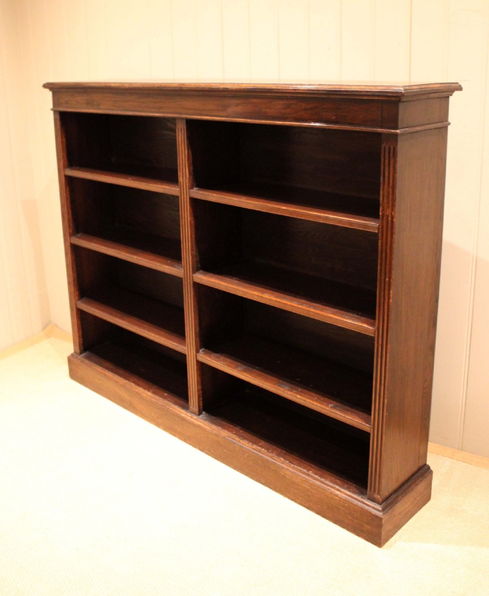 A double-bay open oak library bookcase featuring fluted pilasters, multiple horizontal shelves, a moulded top edge, and a solid plinth base. View VIII