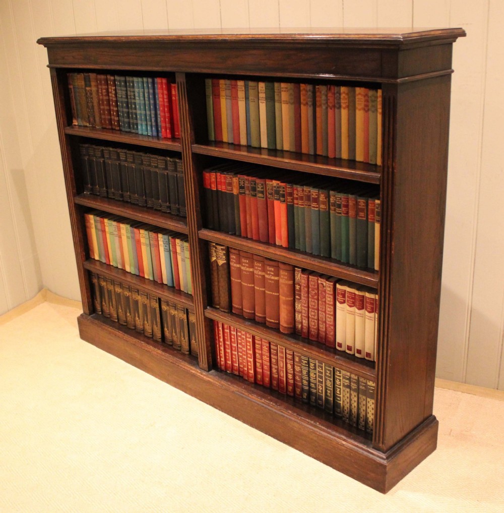 A double-bay open oak library bookcase featuring fluted pilasters, multiple horizontal shelves, a moulded top edge, and a solid plinth base. View XI