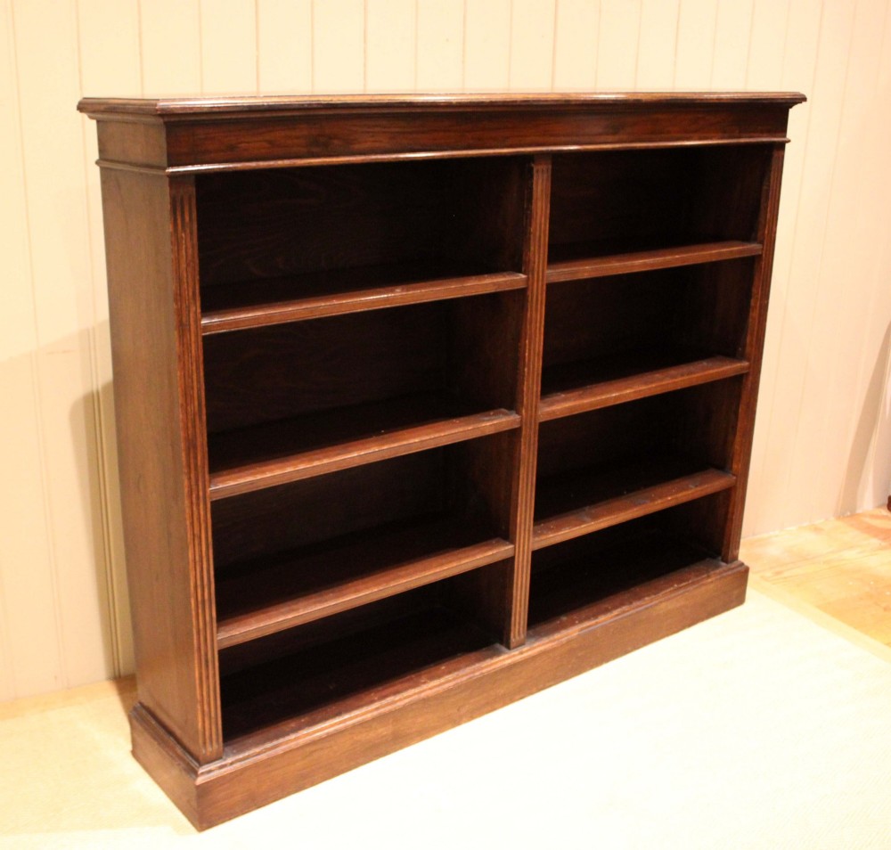 A double-bay open oak library bookcase featuring fluted pilasters, multiple horizontal shelves, a moulded top edge, and a solid plinth base. View XII