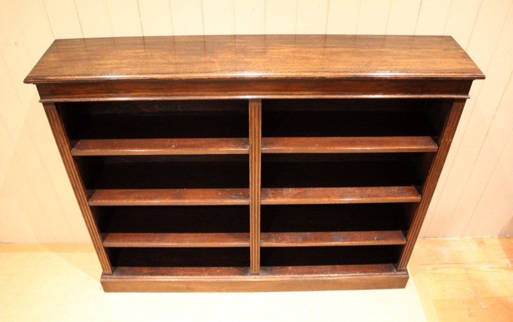 A double-bay open oak library bookcase featuring fluted pilasters, multiple horizontal shelves, a moulded top edge, and a solid plinth base. View XIV