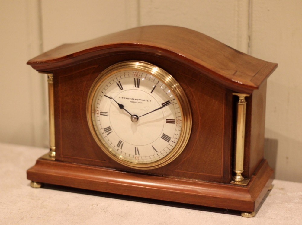 An Edwardian mahogany mantel clock featuring an arched top, brass side columns, brass feet, and a circular white dial with black Roman numerals. View II