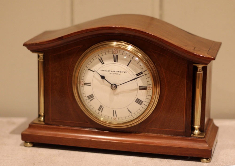 An Edwardian mahogany mantel clock featuring an arched top, brass side columns, brass feet, and a circular white dial with black Roman numerals. View V
