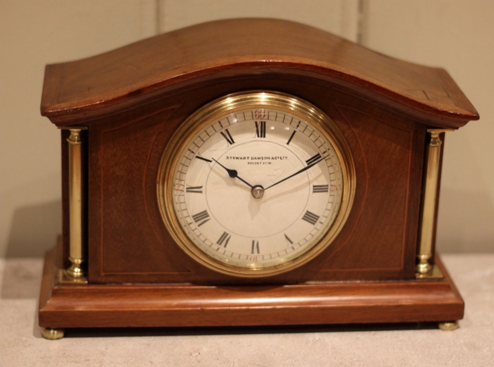An Edwardian mahogany mantel clock featuring an arched top, brass side columns, brass feet, and a circular white dial with black Roman numerals. View VI