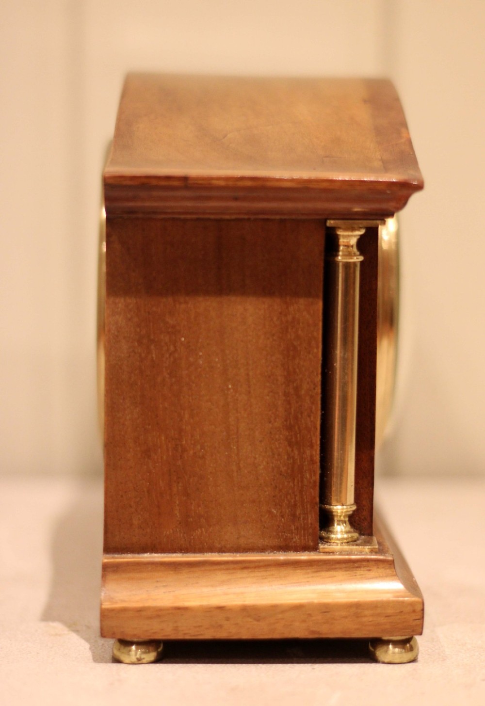An Edwardian mahogany mantel clock featuring an arched top, brass side columns, brass feet, and a circular white dial with black Roman numerals. View VIII