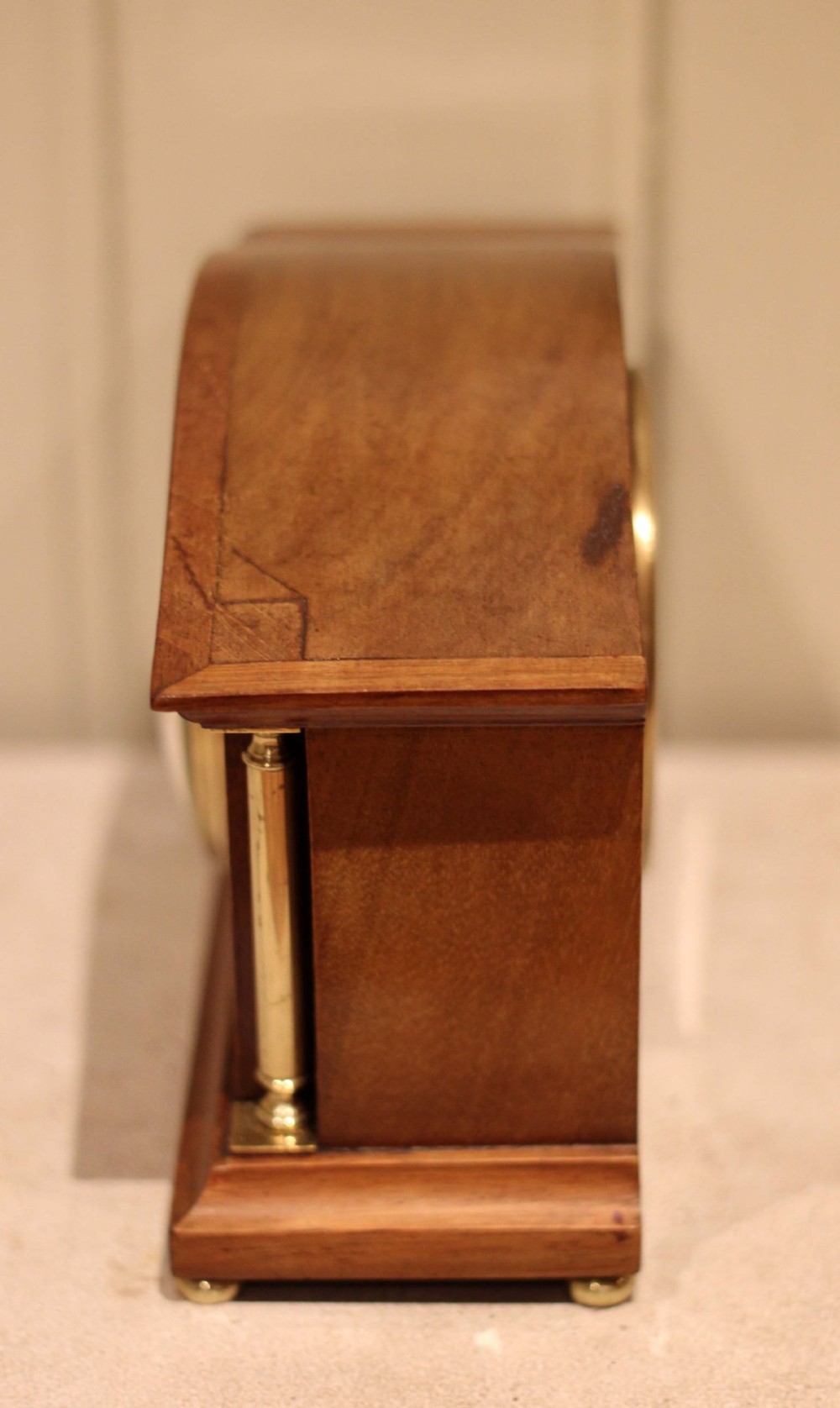 An Edwardian mahogany mantel clock featuring an arched top, brass side columns, brass feet, and a circular white dial with black Roman numerals. View IX