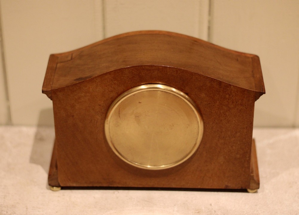 An Edwardian mahogany mantel clock featuring an arched top, brass side columns, brass feet, and a circular white dial with black Roman numerals. View X