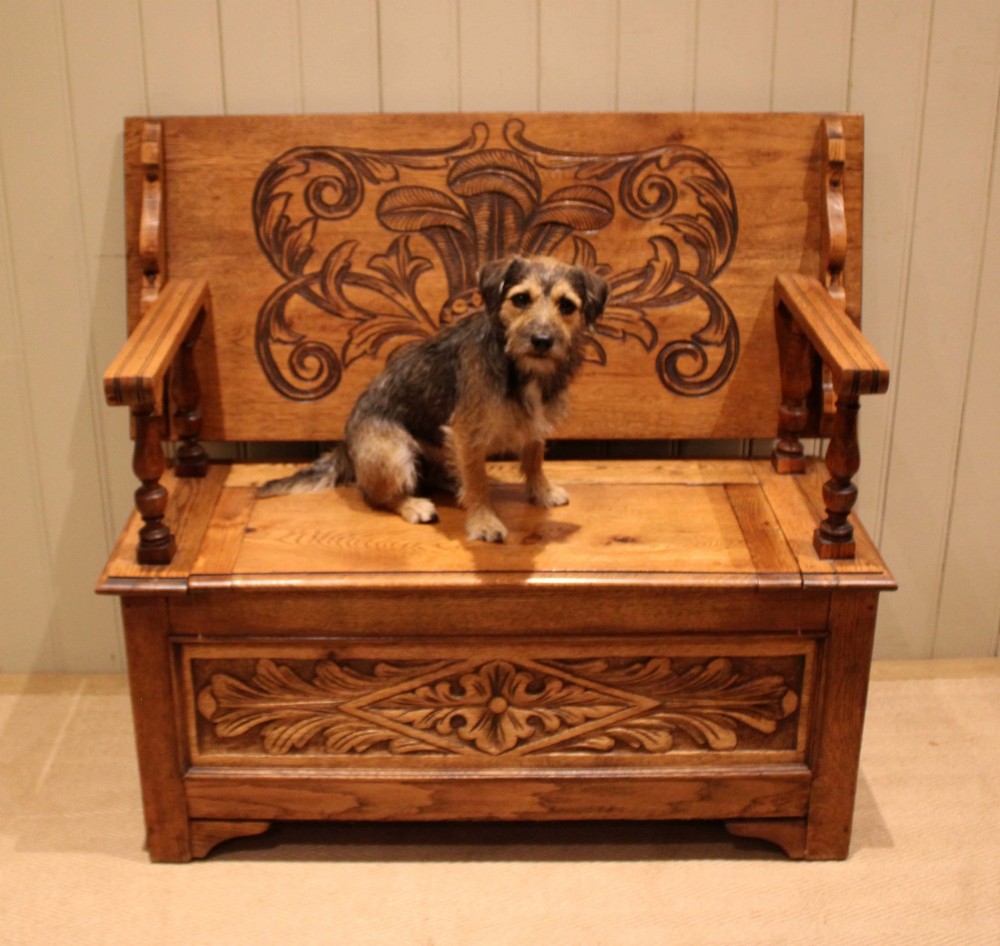 A carved solid oak monks bench featuring a decorative back panel that tilts forward to form a table surface, turned arm supports, and a lift-up storage seat. View VIII