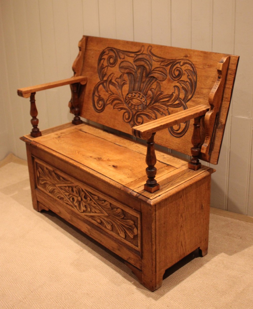 A carved solid oak monks bench featuring a decorative back panel that tilts forward to form a table surface, turned arm supports, and a lift-up storage seat. View XI