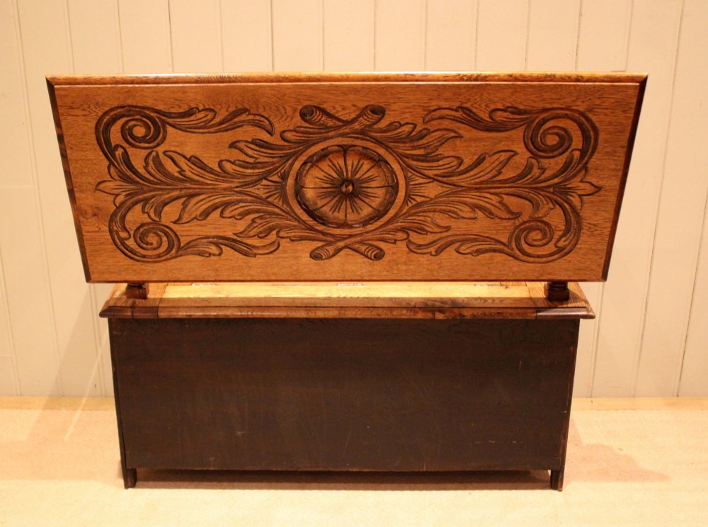 A carved solid oak monks bench featuring a decorative back panel that tilts forward to form a table surface, turned arm supports, and a lift-up storage seat. View XIII