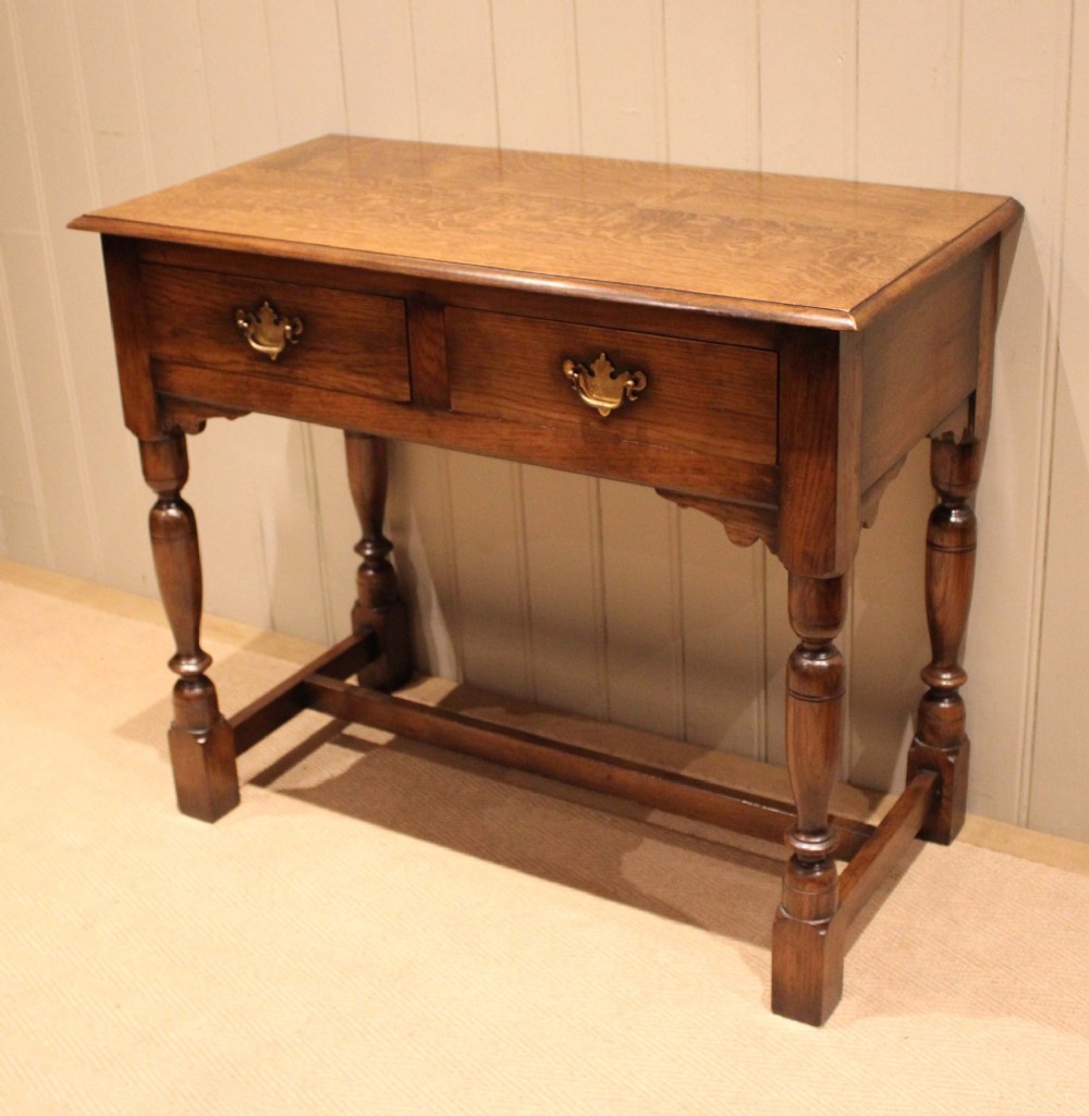 A rectangular solid oak side table featuring a quarter-sawn top, two frieze drawers with brass handles, turned legs, and an H-stretcher base. View II