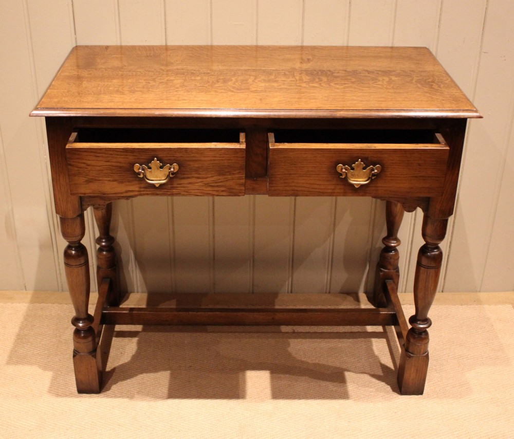 A rectangular solid oak side table featuring a quarter-sawn top, two frieze drawers with brass handles, turned legs, and an H-stretcher base. View III