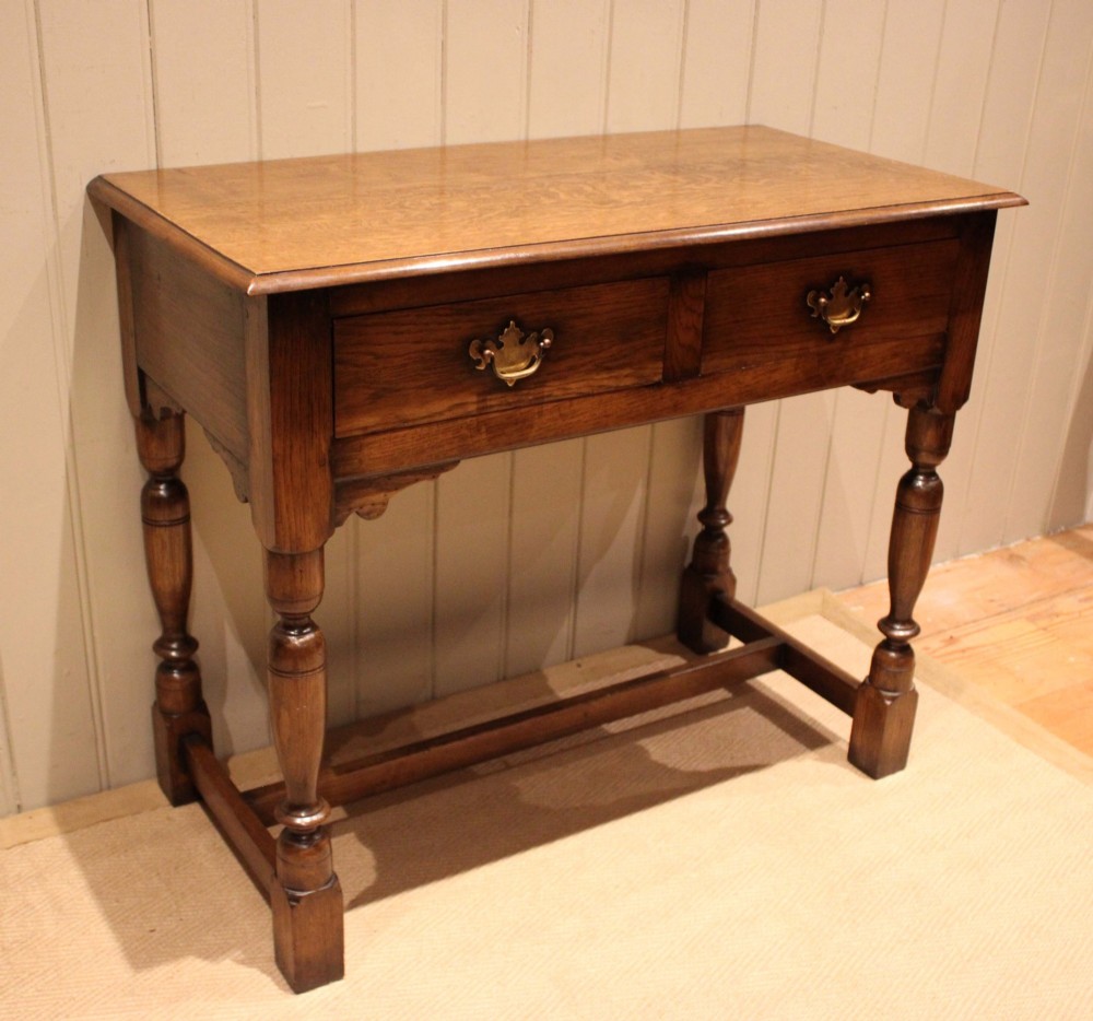 A rectangular solid oak side table featuring a quarter-sawn top, two frieze drawers with brass handles, turned legs, and an H-stretcher base. View IV