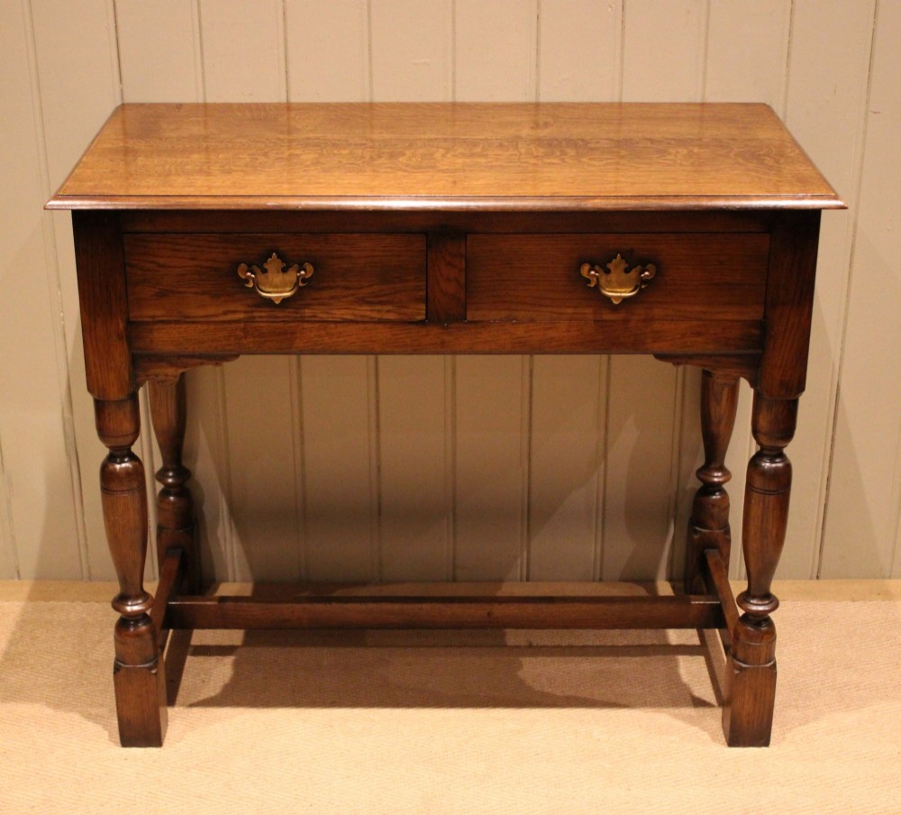 A rectangular solid oak side table featuring a quarter-sawn top, two frieze drawers with brass handles, turned legs, and an H-stretcher base. View V