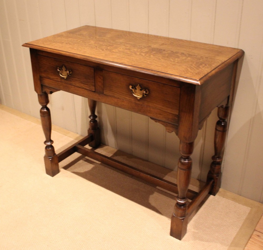 A rectangular solid oak side table featuring a quarter-sawn top, two frieze drawers with brass handles, turned legs, and an H-stretcher base. View VII
