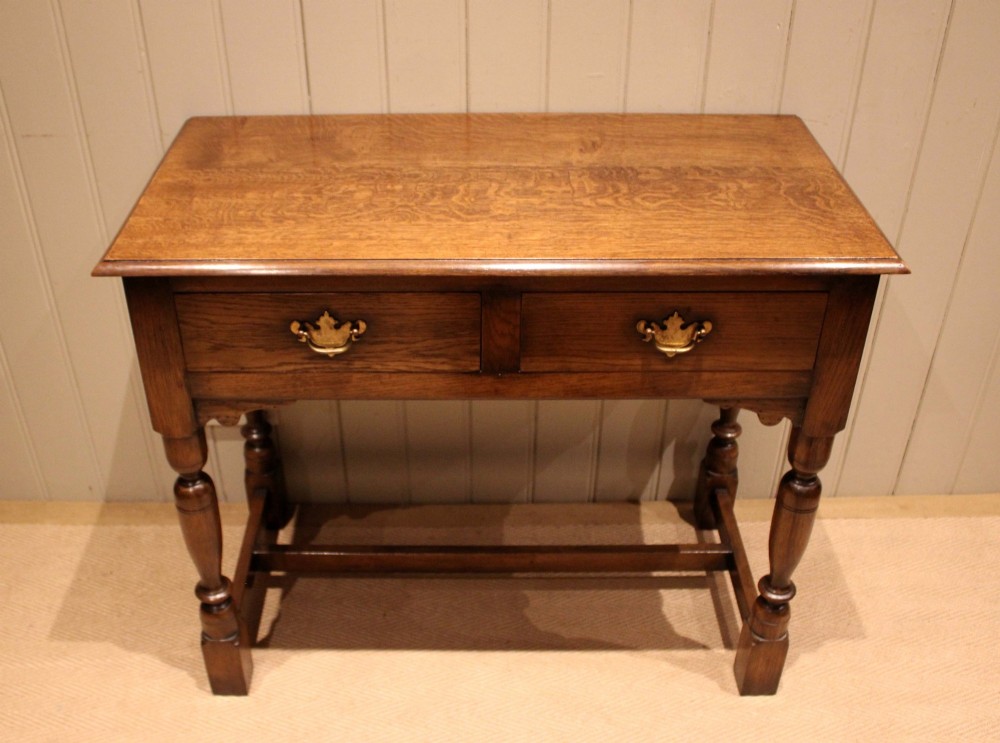 A rectangular solid oak side table featuring a quarter-sawn top, two frieze drawers with brass handles, turned legs, and an H-stretcher base. View VIII