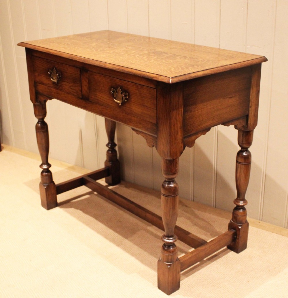 A rectangular solid oak side table featuring a quarter-sawn top, two frieze drawers with brass handles, turned legs, and an H-stretcher base. View XI