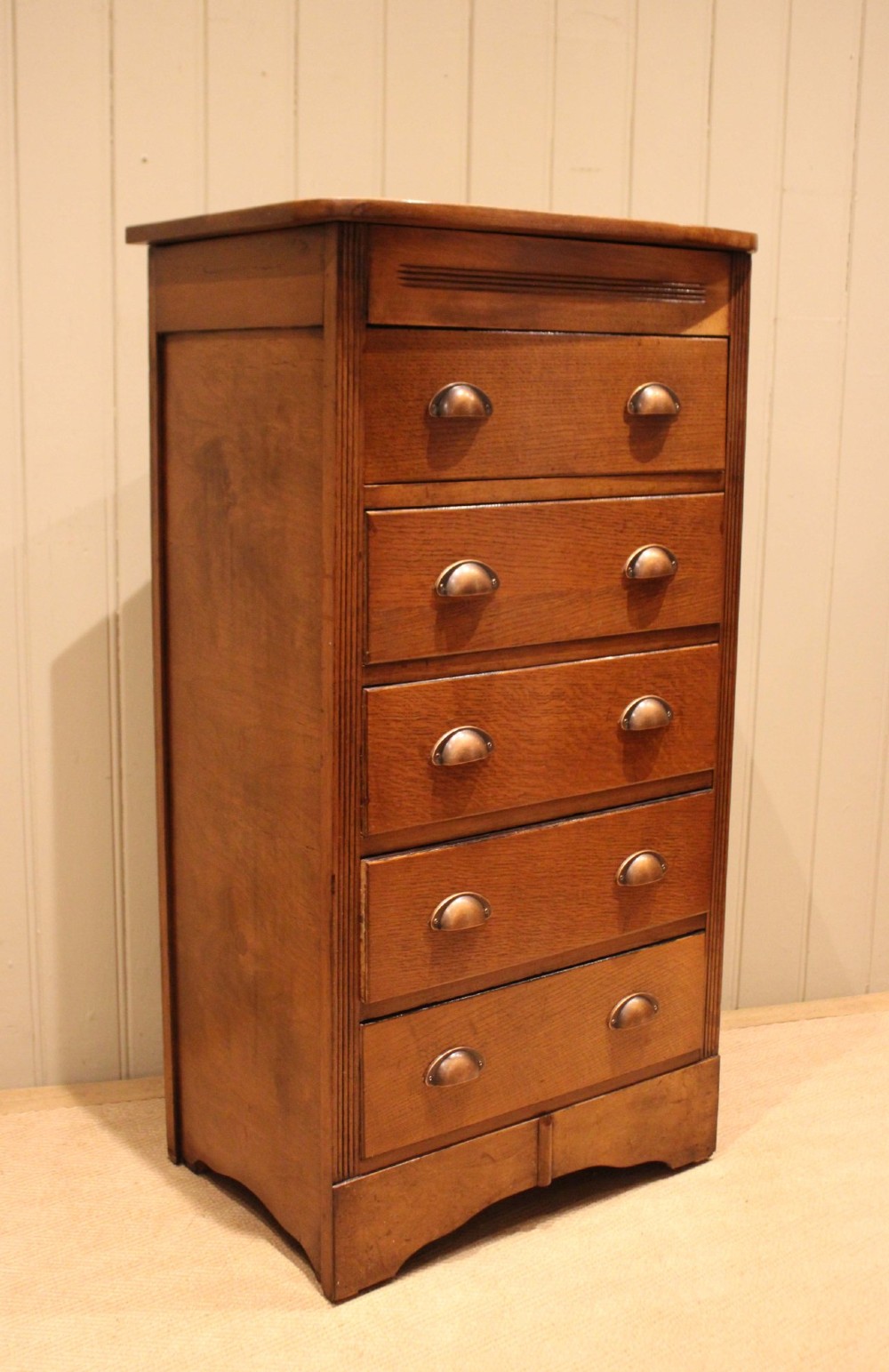 A tall oak chest of drawers featuring five drawers with metal cup handles and reeded side detailing.