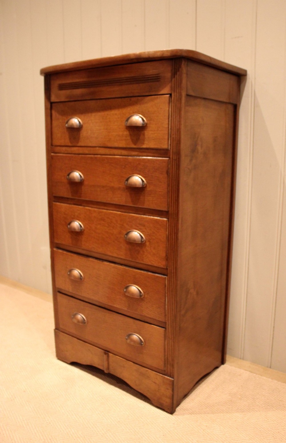 A tall oak chest of drawers featuring five drawers with metal cup handles and reeded side detailing. View III