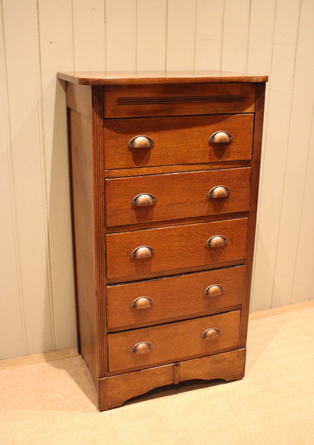 A tall oak chest of drawers featuring five drawers with metal cup handles and reeded side detailing. View IV