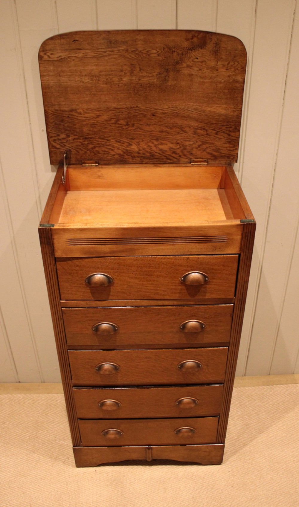 A tall oak chest of drawers featuring five drawers with metal cup handles and reeded side detailing. View V