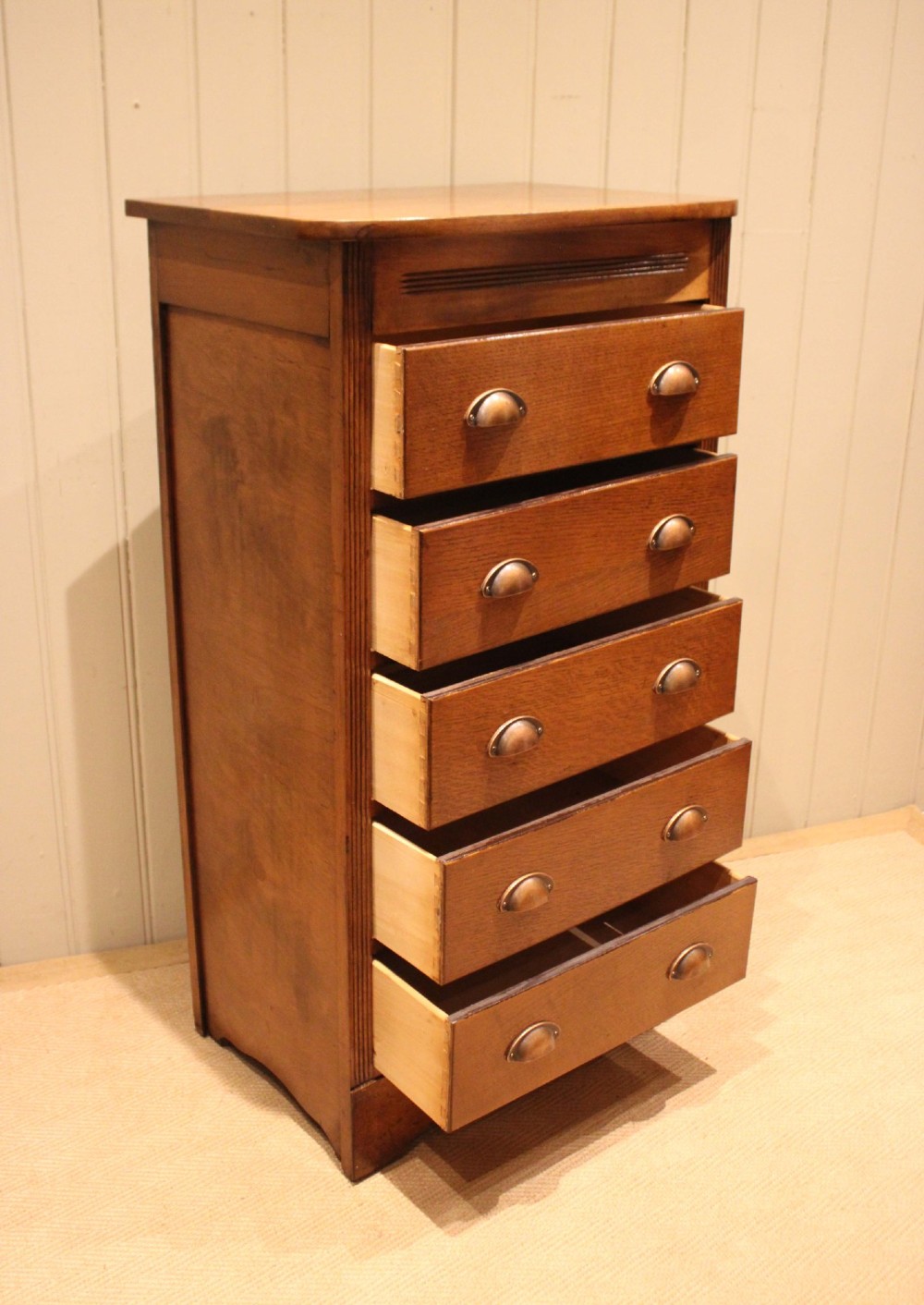 A tall oak chest of drawers featuring five drawers with metal cup handles and reeded side detailing. View VI