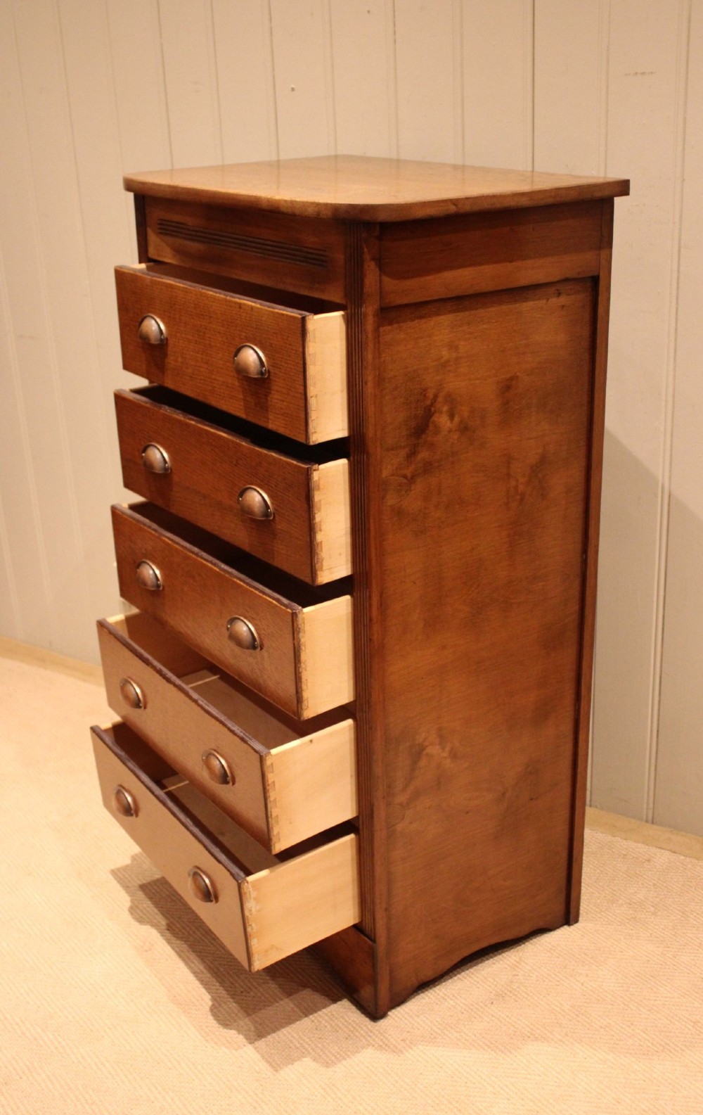 A tall oak chest of drawers featuring five drawers with metal cup handles and reeded side detailing. View VII