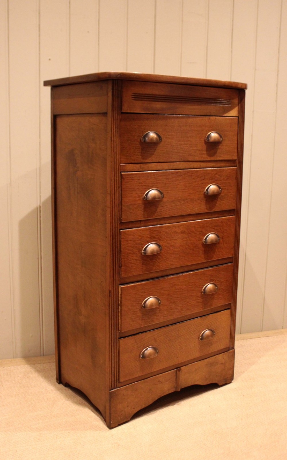 A tall oak chest of drawers featuring five drawers with metal cup handles and reeded side detailing. View VIII