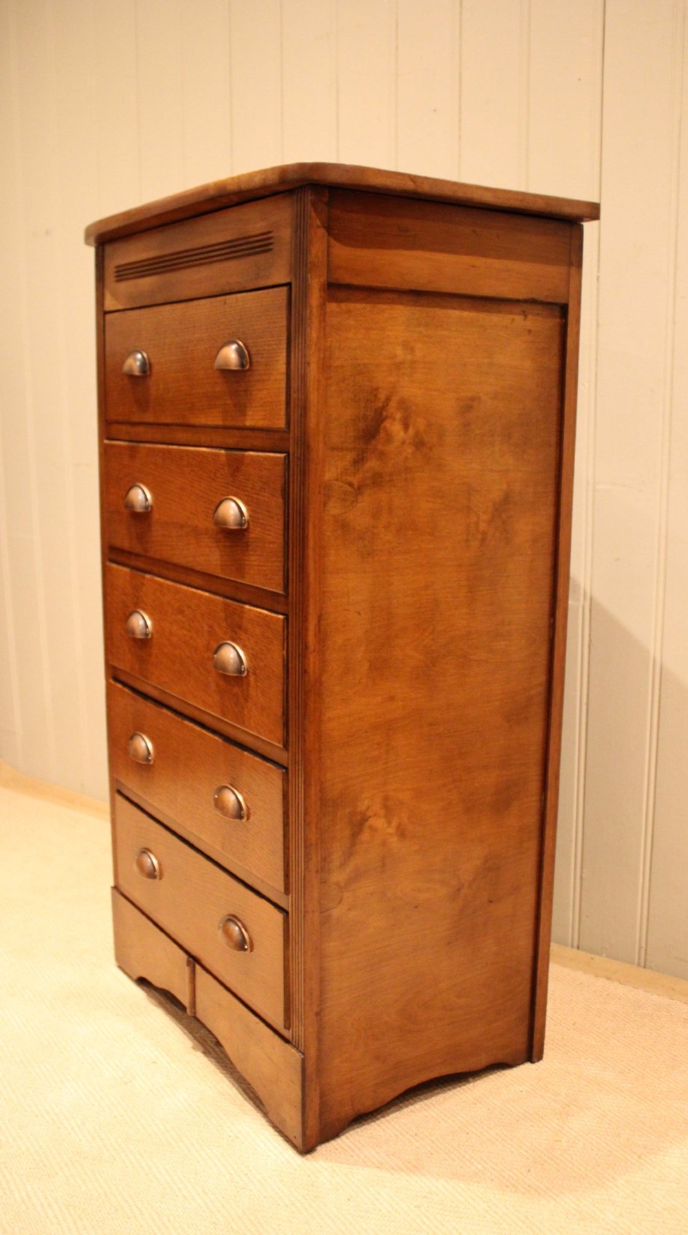A tall oak chest of drawers featuring five drawers with metal cup handles and reeded side detailing. View IX