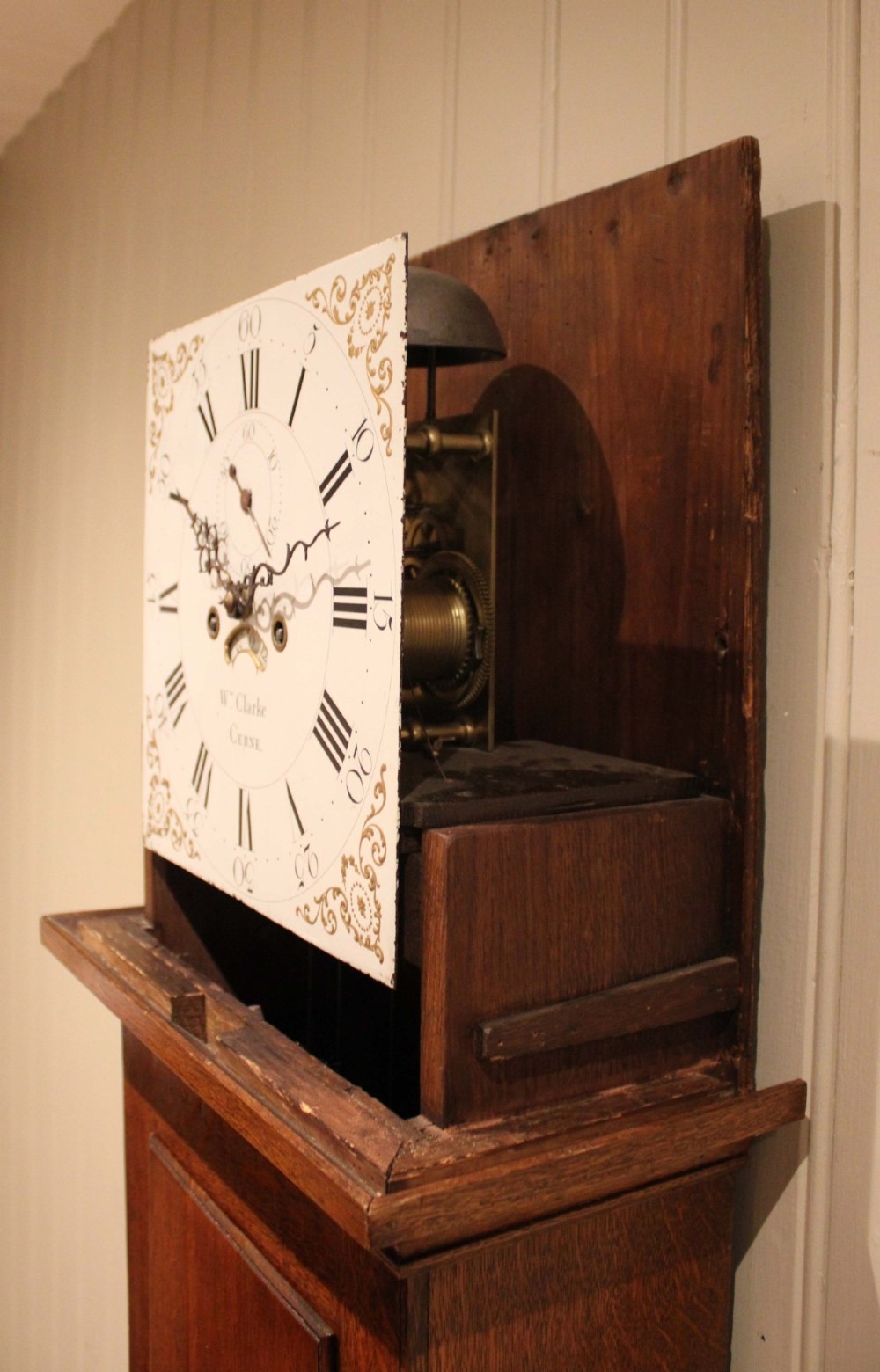 A tall late Georgian oak longcase clock featuring a square painted dial, turned hood columns, and a polished wood trunk. View IX