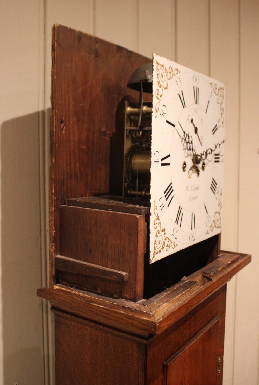 A tall late Georgian oak longcase clock featuring a square painted dial, turned hood columns, and a polished wood trunk. View XI