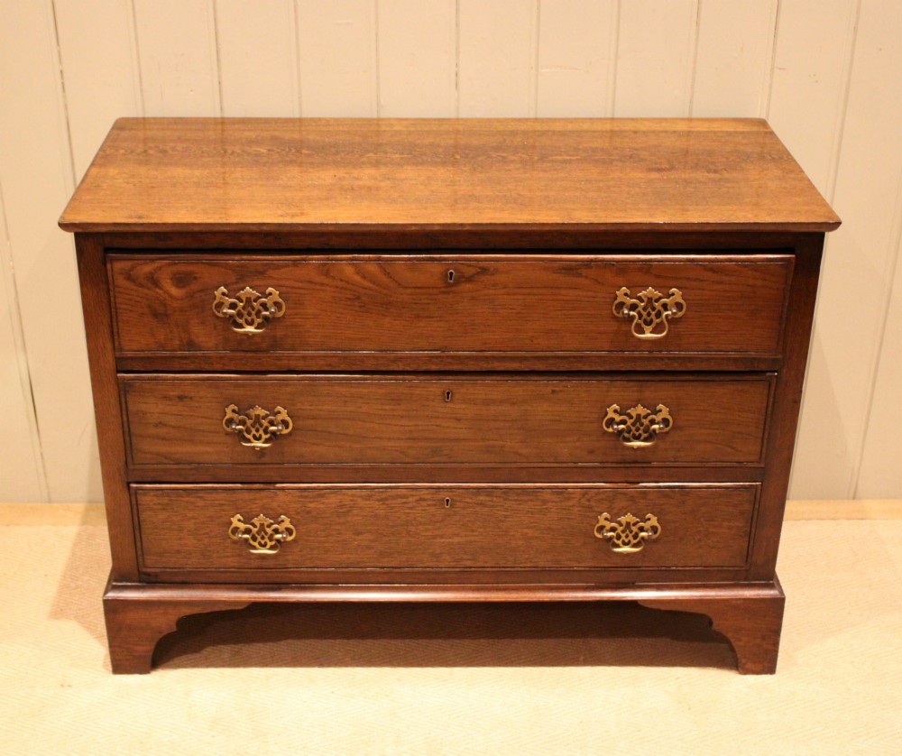 A low Georgian style dark oak chest featuring three full-width drawers with ornate brass handles, set on bracket feet. View II