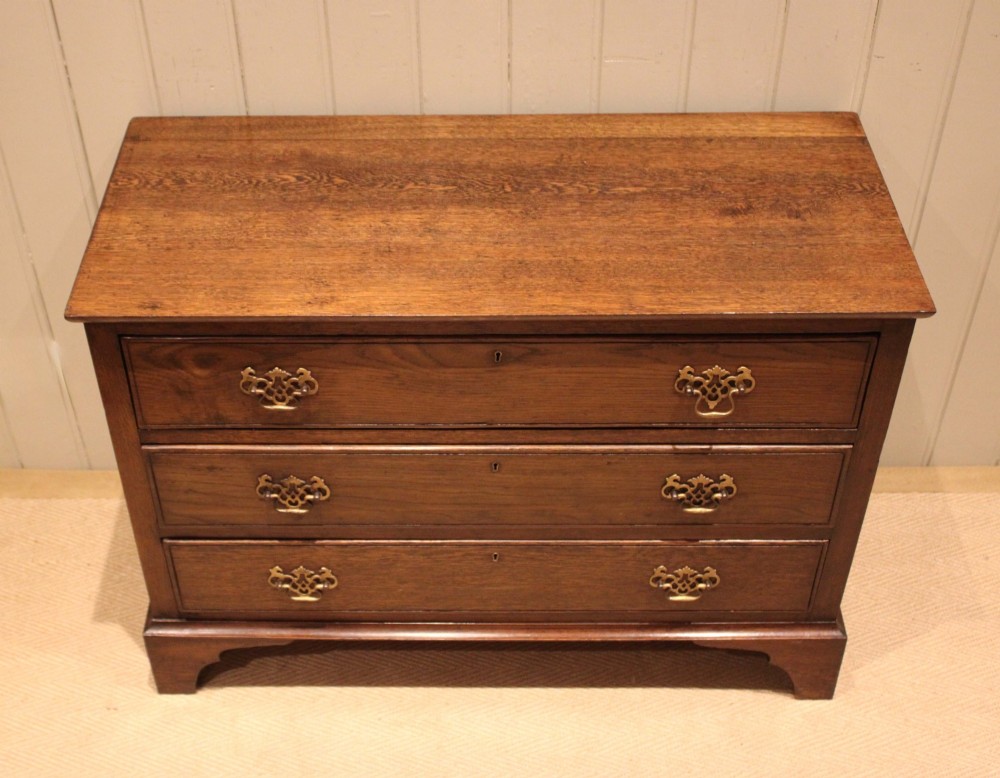 A low Georgian style dark oak chest featuring three full-width drawers with ornate brass handles, set on bracket feet. View IV