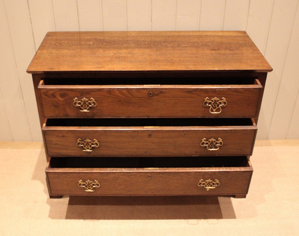 A low Georgian style dark oak chest featuring three full-width drawers with ornate brass handles, set on bracket feet. View VII