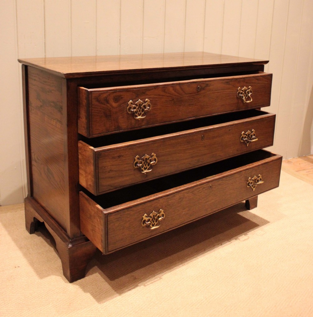 A low Georgian style dark oak chest featuring three full-width drawers with ornate brass handles, set on bracket feet. View VIII