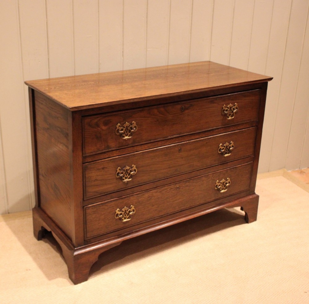 A low Georgian style dark oak chest featuring three full-width drawers with ornate brass handles, set on bracket feet. View IX
