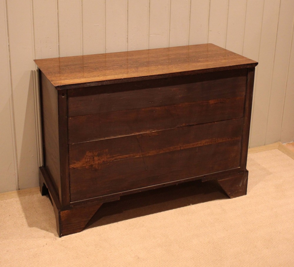 A low Georgian style dark oak chest featuring three full-width drawers with ornate brass handles, set on bracket feet. View XII