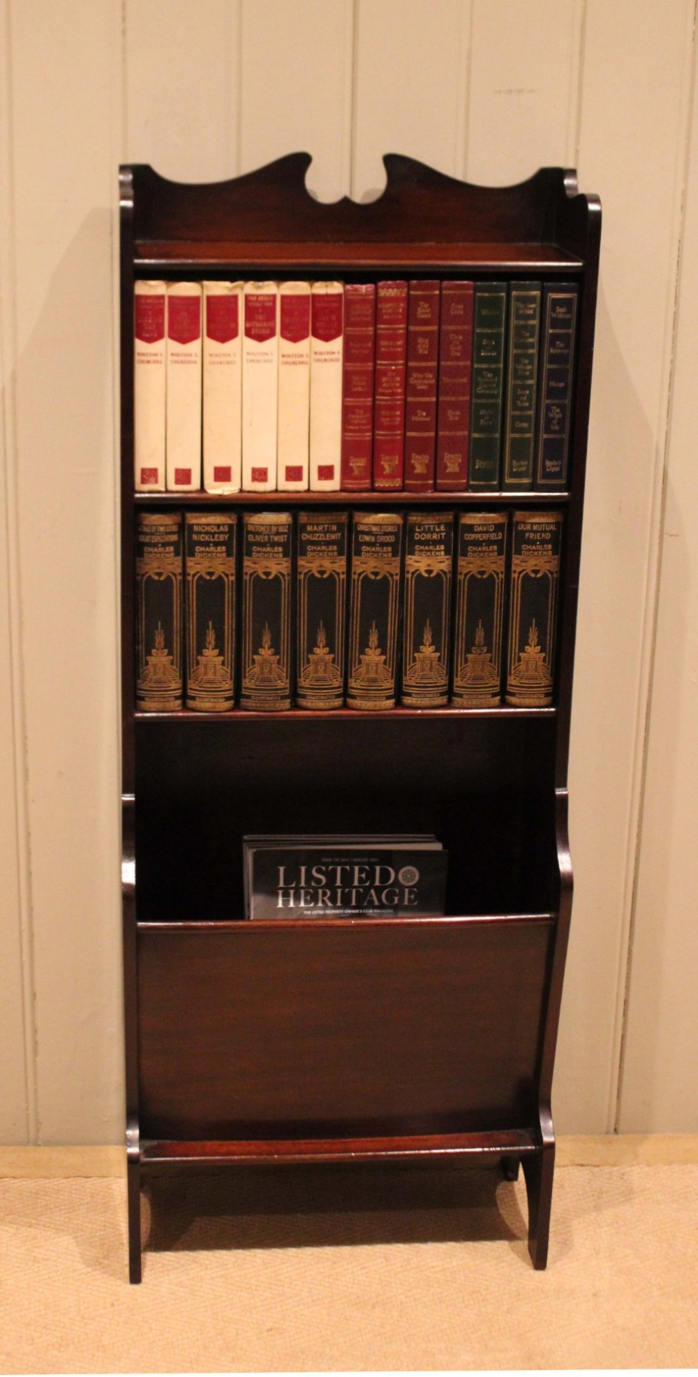 A narrow dark mahogany floor-standing shelf featuring two open upper book shelves and an angled lower magazine trough with a shaped top gallery. View III