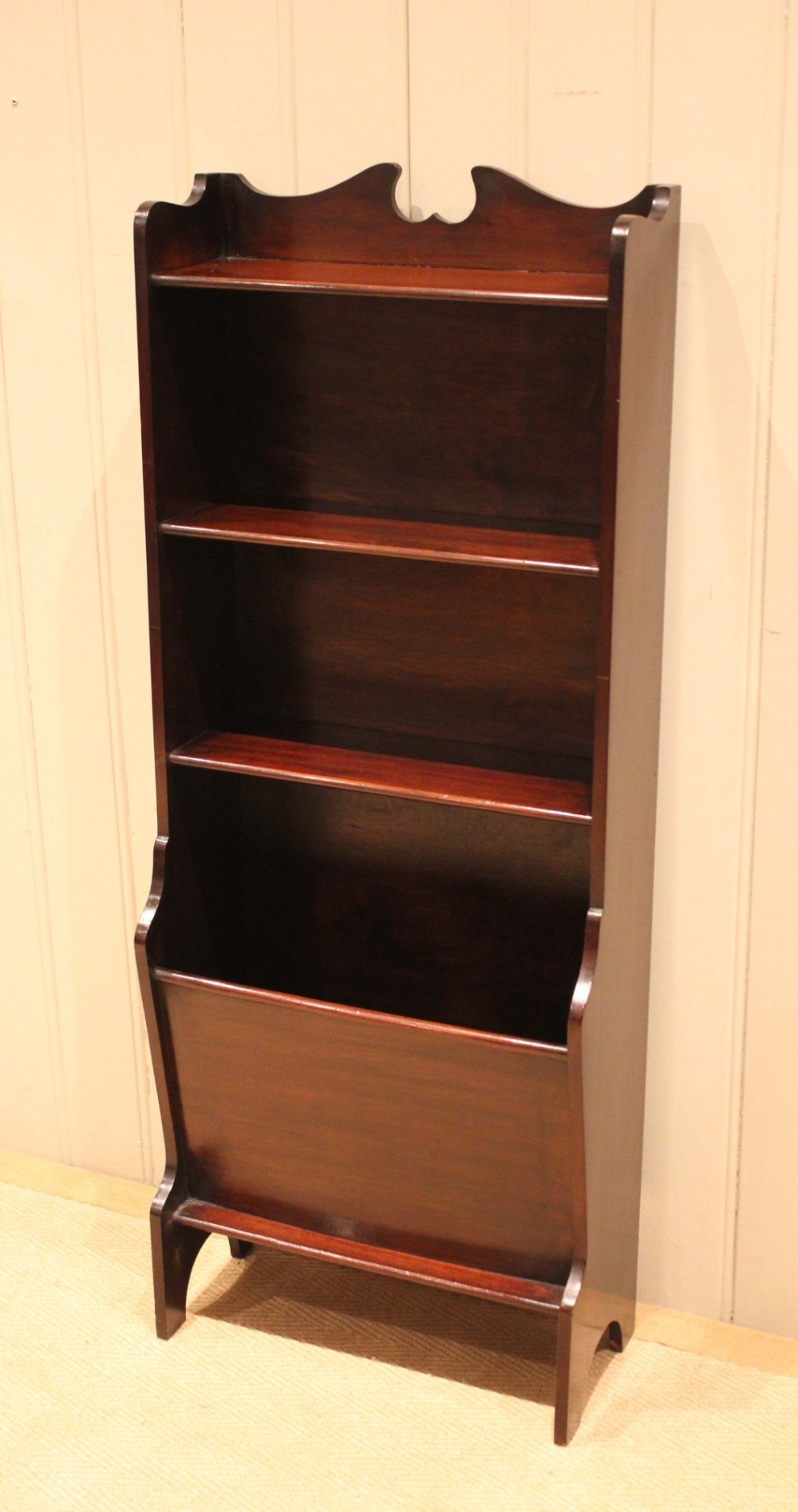 A narrow dark mahogany floor-standing shelf featuring two open upper book shelves and an angled lower magazine trough with a shaped top gallery. View VI