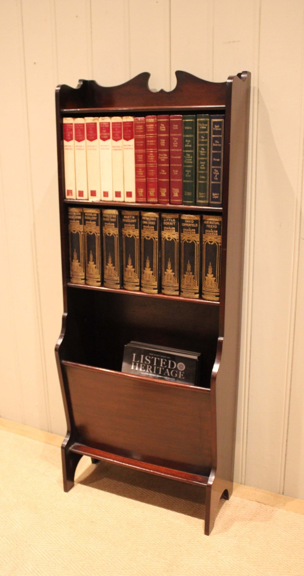A narrow dark mahogany floor-standing shelf featuring two open upper book shelves and an angled lower magazine trough with a shaped top gallery. View VII