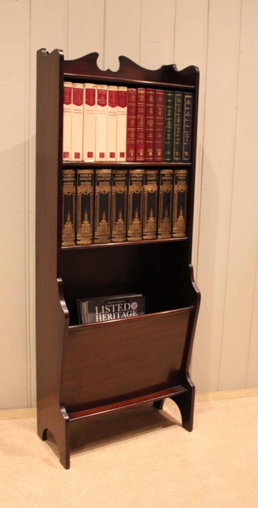 A narrow dark mahogany floor-standing shelf featuring two open upper book shelves and an angled lower magazine trough with a shaped top gallery. View IX