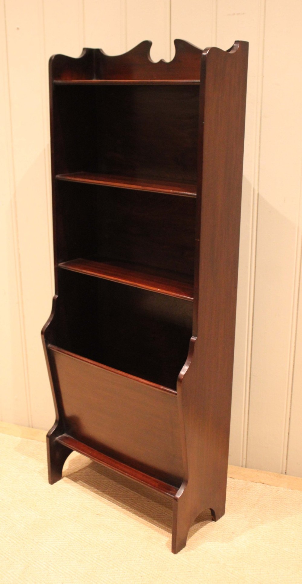 A narrow dark mahogany floor-standing shelf featuring two open upper book shelves and an angled lower magazine trough with a shaped top gallery. View X