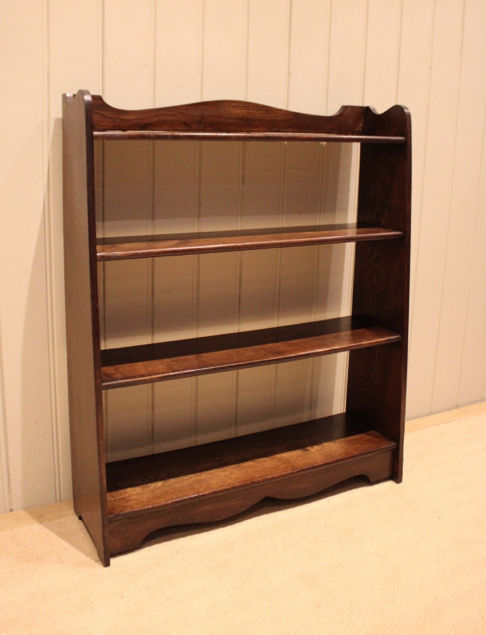 A dark oak open bookcase with three shelves filled with books, featuring a gently curved top cresting and shaped apron. View II
